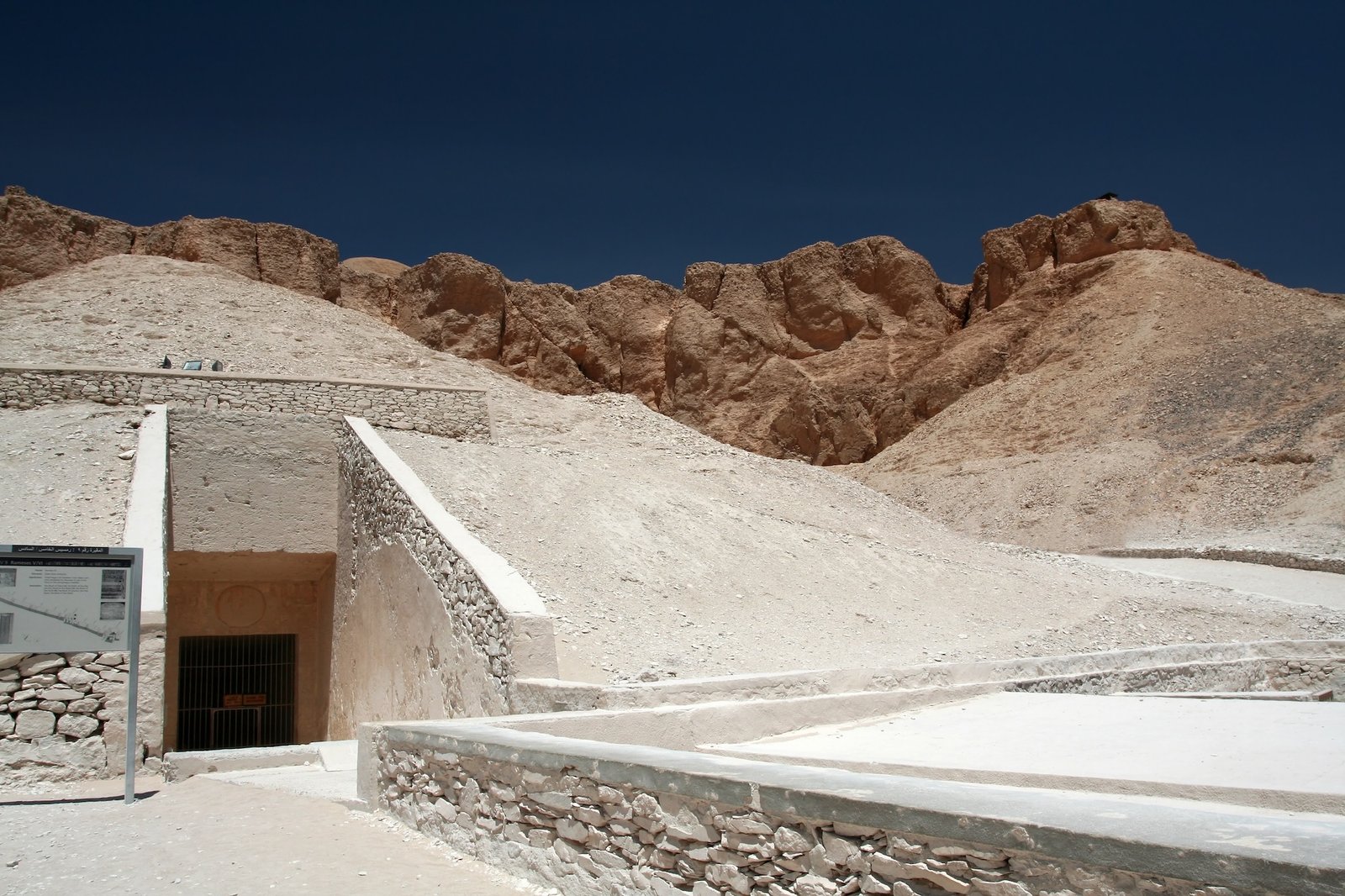 Entrada de tumba antigua en el Valle de los Reyes con escaleras de piedra y acantilados del desierto